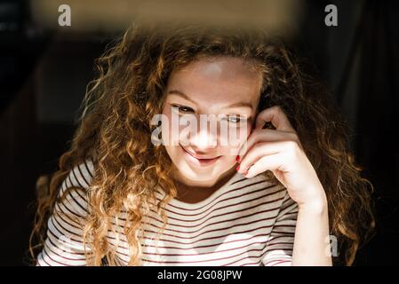 Junge positive hübsche kaukasische Frau, die am frühen Morgen lächelt und mit der Hand ins Gesicht denkt Stockfoto