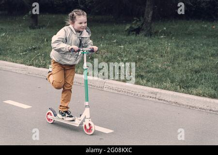 Portrait von aktiven kleinen Kleinkind Mädchen Reiten Roller auf der Straße im Park im Freien am Sommertag. Saisonaler Kindersport. Hochwertige Fotos Stockfoto