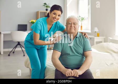 Die fürsorgliche Krankenschwester umarmt den alten Mann, der lächelnd die Kamera während des Besuchs zu Hause anschaut Stockfoto