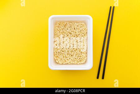 Instant Noodles in einer weißen Packung als traditionelles asiatisches Essen und Essstäbchen auf gelbem Hintergrund, Lebensmittelzusammensetzung, flaches Lay, Draufsicht Stockfoto