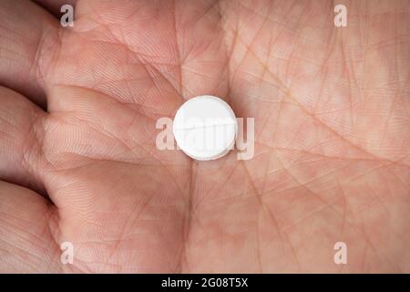 Weiße Pille in der Hand der Männer. Einnahme von Medikamenten. Ein rundes weißes Tablett in der Handfläche. Stockfoto