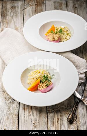 Zwei Portionen Risotto mit Meeresfrüchten auf weißen Tellern. Ei mit geräucherter Makrelenpastete. Honigorange-Tomate. Gourmetküche. Food-Fotografie und Styling. Ich Stockfoto