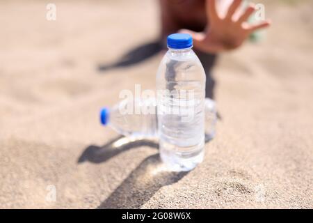 Der Mensch greift nach einer Wasserflasche, die auf Sand steht Stockfoto