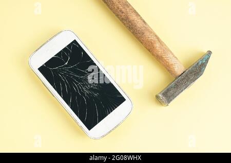 Ein Handy mit einem zerrissenen Bildschirm und einem Hammer auf braunem Hintergrund Stockfoto
