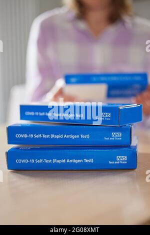Nahaufnahme der Frau zu Hause Lesereianweisungen zur Lieferung von NHS Covid-19 Rapid Antigen Self-Testing Kits Stockfoto
