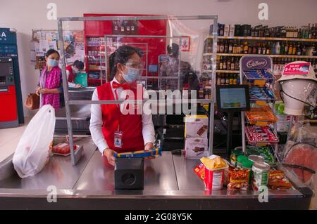 Aufgrund eines Ausbruchs von COVID - 19 trägt ein Kassierer im Supermarkt an einem Kassenschalter eine schützende Gesichtsmaske und einen Gesichtsschutz, während er während der Coronavirus-Pandemie hinter einem selbstgemachten Plastikschild steht. Phnom Penh, Kambodscha. Dezember 2020. © Kraig Lieb Stockfoto