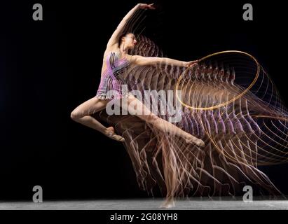 Porträt eines jungen Mädchen rhythmische Turnerin in Bewegung und Aktion isoliert in gemischtem Licht auf dunklem Hintergrund. Stockfoto