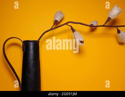 Papierblume auf einer schwarzen Metallvase mit gelbem Hintergrund Stockfoto