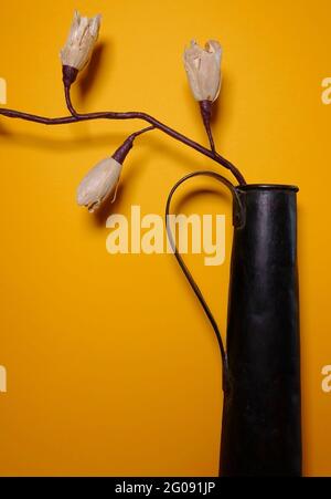 Papierblume auf einer schwarzen Metallvase mit gelbem Hintergrund Stockfoto