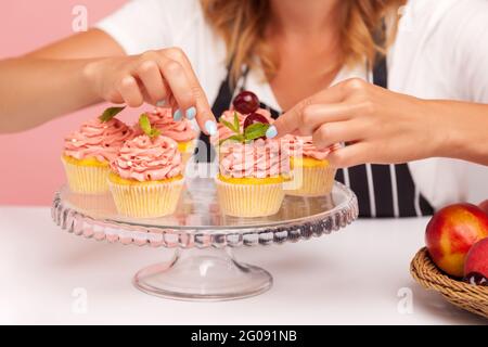 Nahaufnahme von vielen süßen Cupcakes auf Grasplatten, Bäcker dekorieren süße leckere Muffins, hausgemachtes Gebäck, das sich zum Servieren bereitmacht. Innenstudio s Stockfoto