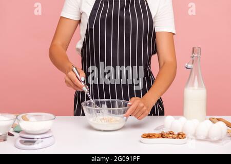 Zugeschnittenes Bild des Bäckers in schwarz gestreifter Schürze Mischen von Teig mit Corolla, Herstellung von Bäckerei, hausgemachtem Gebäck, Konditor Zubereitung von Kuchen. Studio-Zimmer im Innenbereich Stockfoto