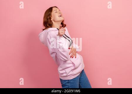 Porträt eines positiv aufgeregt lockig behaarten Teenagers im Hoodie, das laut den Bauch hält und mit dem Finger auf dich zeigt, Spott. Studio-Zimmer im Innenbereich Stockfoto