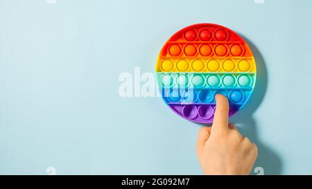 Die Hand eines Kindes drückt auf Pop-it-Spielzeugsilikon auf blauem Hintergrund. Anti-Stress-Spielzeug, ein Trend bei Kinderspielzeug. Stockfoto