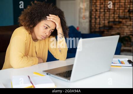 Müde afrikanische Freiberuflerin fühlt sich Stress, hält die Stirn und blickt verzweifelt auf den Laptop-Bildschirm, hat finanzielle Probleme oder Probleme mit dem Projekt, depressive arbeitslose Frauen können keinen Job finden Stockfoto