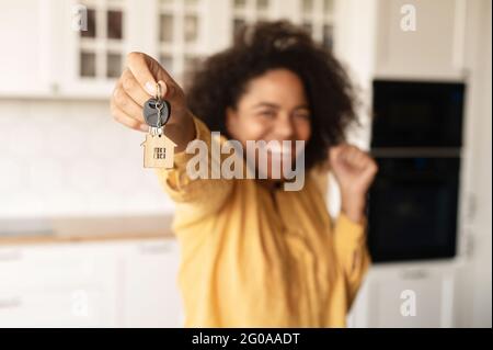 Fröhliche afroamerikanische Frau hält Schlüssel mit Schmuckkeller in Form eines kleinen niedlichen Hauses, selektiver Fokus auf die Schlüssel Stockfoto