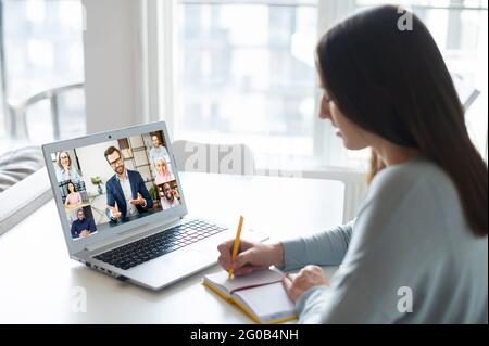 Junge Frau, die mit einem Laptop online Kurse oder Webinare anschaut, nimmt Studentin an Videokonferenzen Teil, notiert, schreibt, E-Learning und lernt aus der Ferne Stockfoto