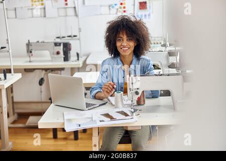 Lächelnde afroamerikanische Modedesignerin zeichnet am Arbeitsplatz Kleider-Modelle Stockfoto