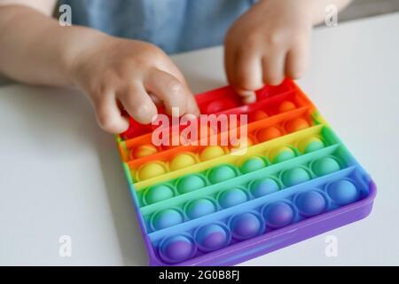 Bunte Antistress Sinnesspielzeug Fidget Push Pop es in die Hände des Kindes auf weißen Tisch Stockfoto