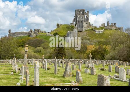 Grabsteine auf dem Friedhof von Corfe Castle mit Ruinen von Corfe Castle, die sich über den Purbeck Hills in Dorset, England erheben Stockfoto