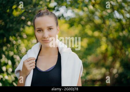 Schöne dunkelhaarige Europäerin trägt schwarzes T-Shirt und weißen Pullover über den Schultern schaut direkt auf die Kamera hat regelmäßige Outdoor-Training Spaziergänge in Stockfoto