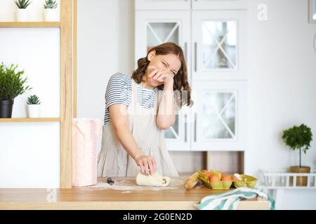 Glückliche Hausfrau mit rohem Teig beim Kochen am Tisch in der Küche Stockfoto