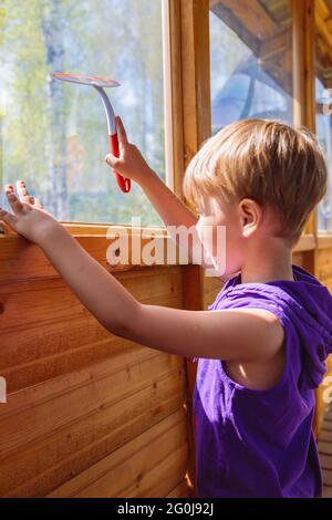 Das Kind wäscht die Fenster mit einer speziellen Bürste. Ein Kind mit blonden Haaren. Stockfoto