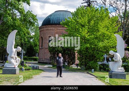 Der ältere Mann steht neben dem Marmorengel am Eingang des Friedhofs St. Hedwig, Alter Domfriedhof St. Hedwig, Berlin. Stockfoto