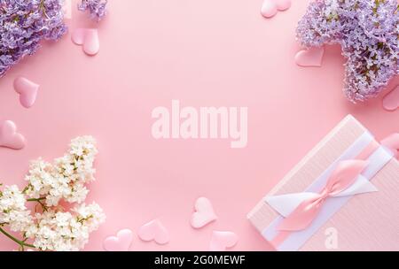 Bouquet von schönen weißen und lila Flieder, Geschenkbox und Herzen auf rosa Hintergrund. Draufsicht. Festliche Grußkarte mit Pfingstrose für Hochzeiten, Valentin Stockfoto
