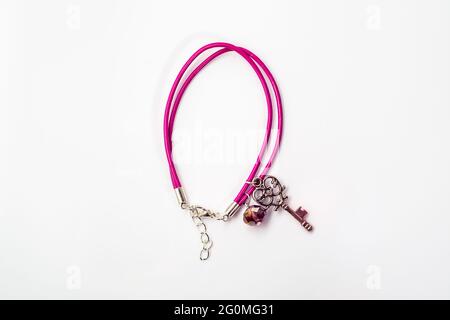 Nahaufnahme eines handgefertigten Armbandes aus rosa Leder, Kristallglas und Anhänger in Form Schlüssel isoliert auf weißem Hintergrund, Draufsicht. Stockfoto