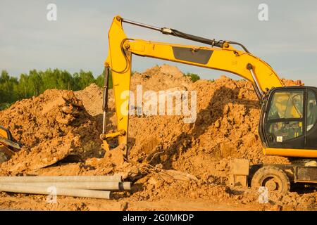 Gelber Bagger bei Erdarbeiten auf der Baustelle. Bagger graben den Boden für das Fundament und für die Verlegung von Kanalrohren Fernwärme. Ea Stockfoto