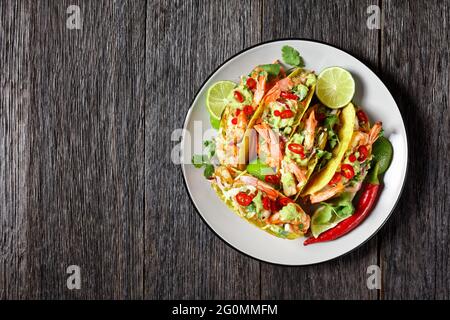 taco-Muscheln mit gegrillten Garnelen, Kohlsalat, Limette und Guacamole auf einem Teller auf einem Holztisch, flach liegend, freier Platz Stockfoto