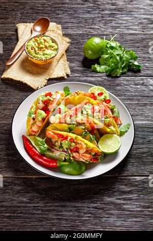 taco-Muscheln mit Garnelen, Kohlsalat, Limette und Guacamole auf einem Teller, vertikale Ansicht Stockfoto