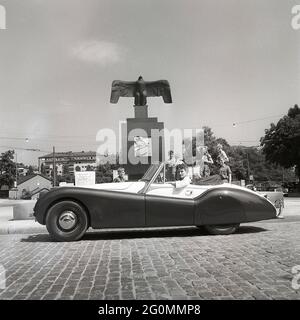 Fahren in den 1950er Jahren. Eine junge Frau in einem offenen Cabriolet des Jaguar XK120. Ein britischer Sportwagen, der als futuristisch anmutet. Die Zahlen 120 geben die Höchstgeschwindigkeit des Fahrzeugs an, 120 mph/193 km/h. Das Auto war ein Zweisitzer mit einer Aluminium-Chasse. Es wurde in insgesamt 12078 Autos hergestellt. Auf der Straße vom Flugdenkmal von Carl Milles auf Karlaplan in Stockholm abgebildet. Eine Hommage an schwedische Piloten und geflügelte Pioniere. Schweden 1953. ref. BL109-2 Stockfoto