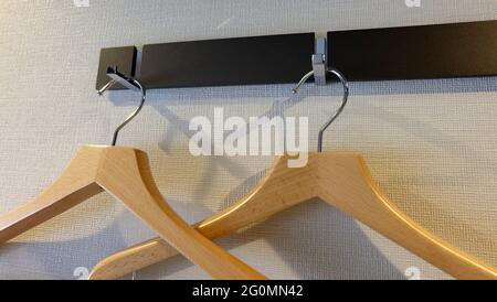 Nahaufnahme von zwei Kleiderbügeln aus Holz mit Metallhaken, die an einem Wandhalter hängen. Stockfoto