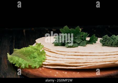 Stapel von Pitabrot und Salatblättern auf einem Holzbrett. Stockfoto