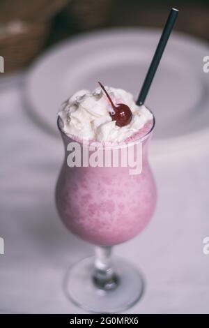 Teilweise verschwommenes Glas mit Beerenmilchshake mit Stroh, Schlagsahne und Cocktailkirsche. Vertikal Stockfoto