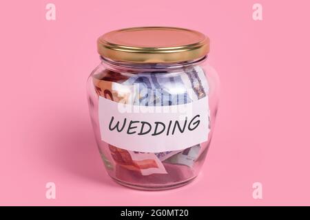 Geldschachtel mit Wort HOCHZEIT auf Haftnotizpapier. Euro-Banknoten im Glas-Geldbecher mit Sparetikett, finanziell, sparend. JAR voller Bargeld, sparen Stockfoto