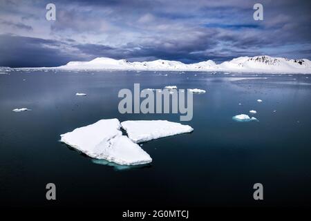 Schwimmende Bruchstücke von Packeis im arktischen Meer, mit den schneebedeckten Bergen von Spitzbergen in der Ferne. Tagsüber Seestücke . Stockfoto