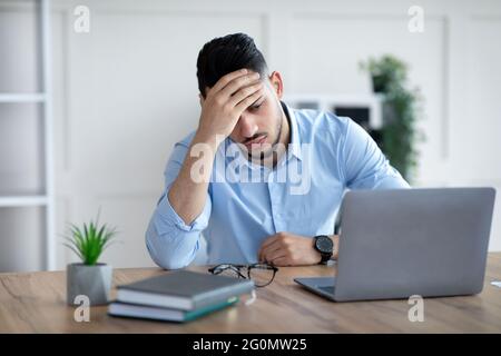 Müder, tausendjähriger arabischer Geschäftsmann, der an Kopfschmerzen am Schreibtisch im modernen Büro leidet Stockfoto