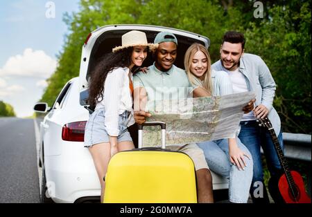 Reisen mit Freunden. Glückliche multirassische junge Menschen sitzen in offenen Kofferraum, überprüfen Karte, Spaß Roadtrip Stockfoto