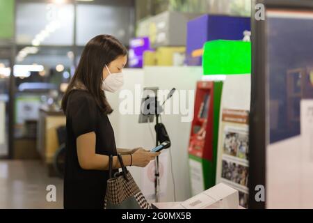 Asiatische Frau in Schutzmaske mit Handy scannen qr-Code. Stockfoto