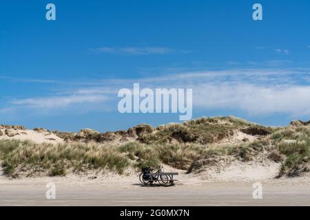 Zwei Fahrräder parkten vor einer großen Sanddüne, die mit Gräsern und Schilf unter blauem Himmel bedeckt war Stockfoto