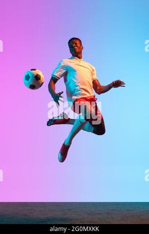 Porträt eines afrikanischen Fußballprofi, der isoliert auf einem blau-rosa Hintergrund in Neonlicht steht. Rückansicht Stockfoto