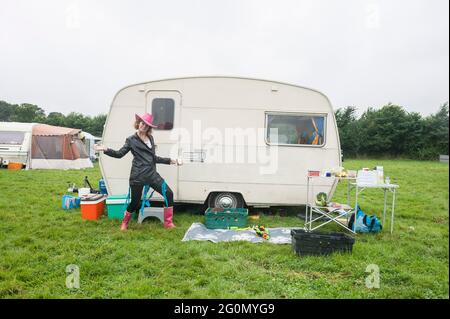 Vor einem Wohnwagen / Wohnmobil auf einem Fest auf einem Feld stehen. Stockfoto