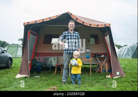 Vor einem Wohnwagen / Wohnmobil auf einem Fest auf einem Feld stehen. Stockfoto