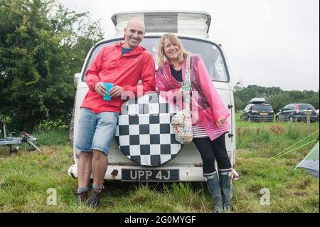 Vor einem Wohnwagen / Wohnmobil auf einem Fest auf einem Feld stehen. Stockfoto