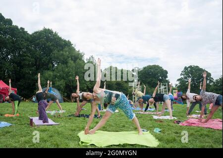 Eine Gruppe von Menschen, die einen Yogakurs machen und auf einem Festival draußen auf einem Feld trainieren. Stockfoto