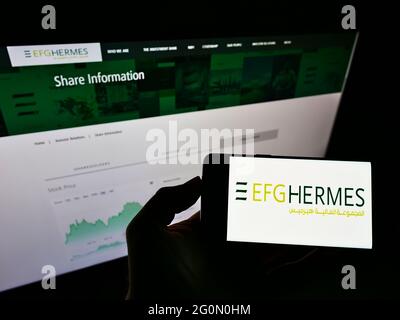 Person, die das Smartphone mit dem Logo der ägyptischen Finanzgesellschaft EFG Hermes Holding S.A.E. auf dem Bildschirm vor der Website hält. Konzentrieren Sie sich auf die Telefonanzeige. Stockfoto