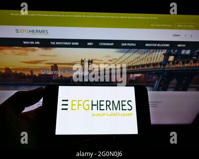 Person, die ein Mobiltelefon mit dem Logo des ägyptischen Finanzunternehmens EFG Hermes Holding SAE auf dem Bildschirm vor der Webseite hält. Konzentrieren Sie sich auf die Telefonanzeige. Stockfoto