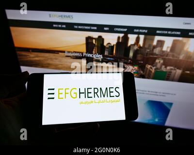 Person, die Mobiltelefon mit dem Logo des ägyptischen Finanzunternehmens EFG Hermes Holding SAE auf dem Bildschirm vor der Webseite hält. Konzentrieren Sie sich auf die Telefonanzeige. Stockfoto